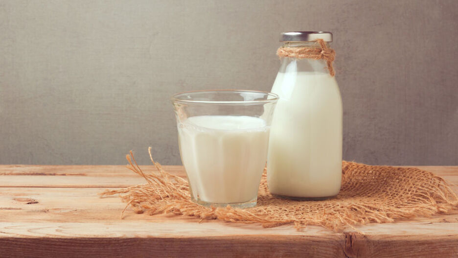 Ein Glas und eine Flasche Milch stehen auf einem Holzbrett.