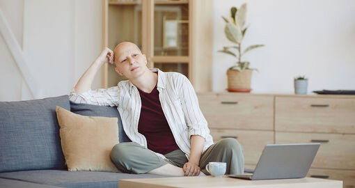 Person mit Glatze sitzt auf der Couch und schaut in die Ferne.