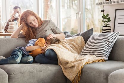 Eine Frau tröstet ihr erkältetes Kind. Beide liegen dabei auf der Couch. 