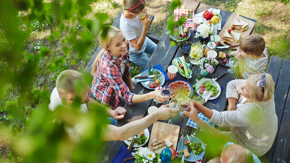 Familie sitzt auf einem gedeckten Tisch in der Natur und genießt das gemeinsame Essen